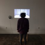 A person with headphones on watching a video being projected onto the wall