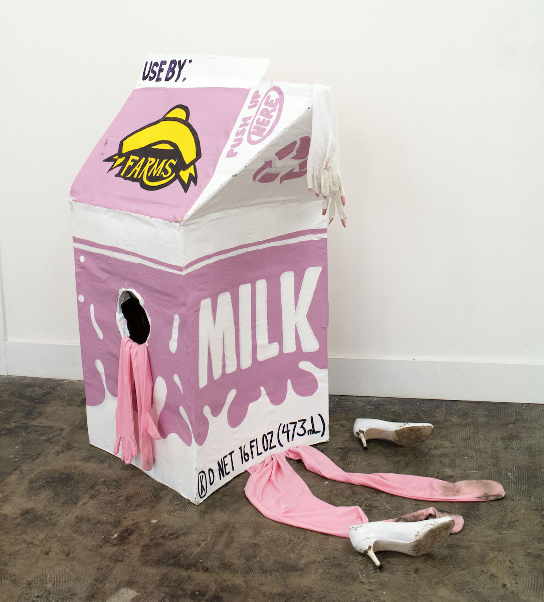 A lifesize single-serve pink and white and yellow cart on of milk with pink gloves and white shoes nearby