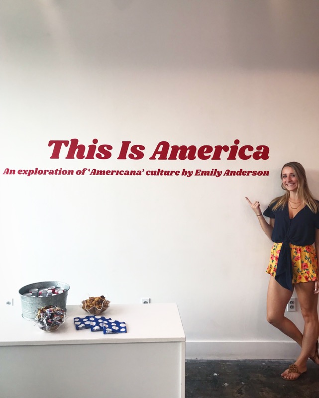 A young woman posing for a photo next to the "This is America" text