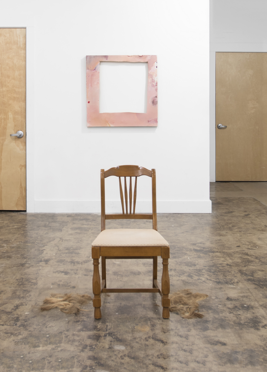 A chair on the gallery floor, a pink square frame on the wall behind
