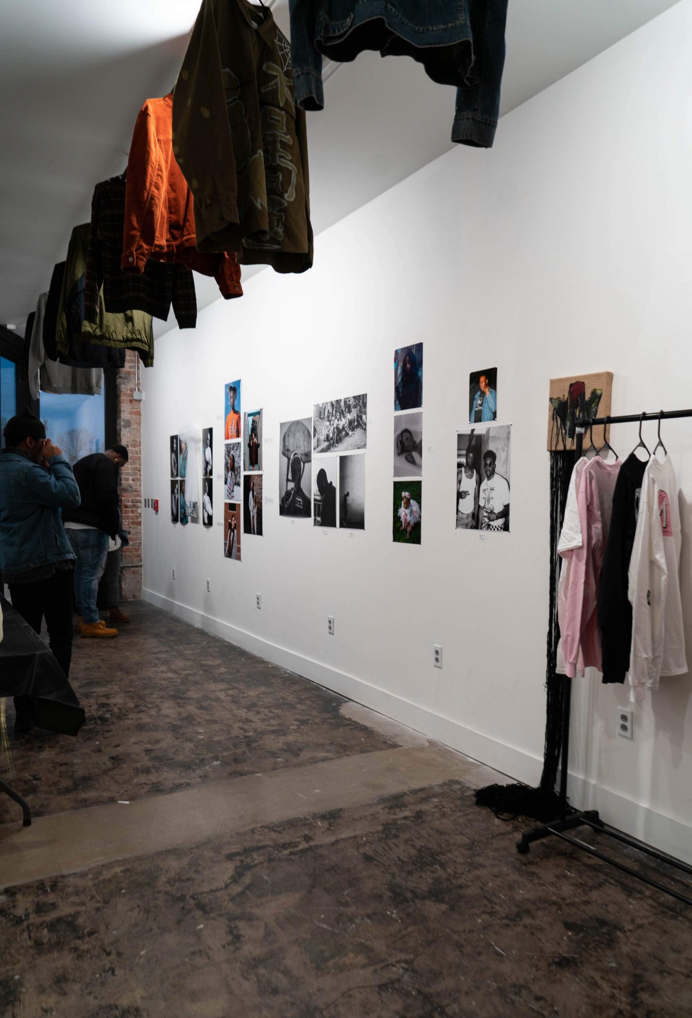 A photo of art on the walls with a clothing rack on the right and coats hanging from above