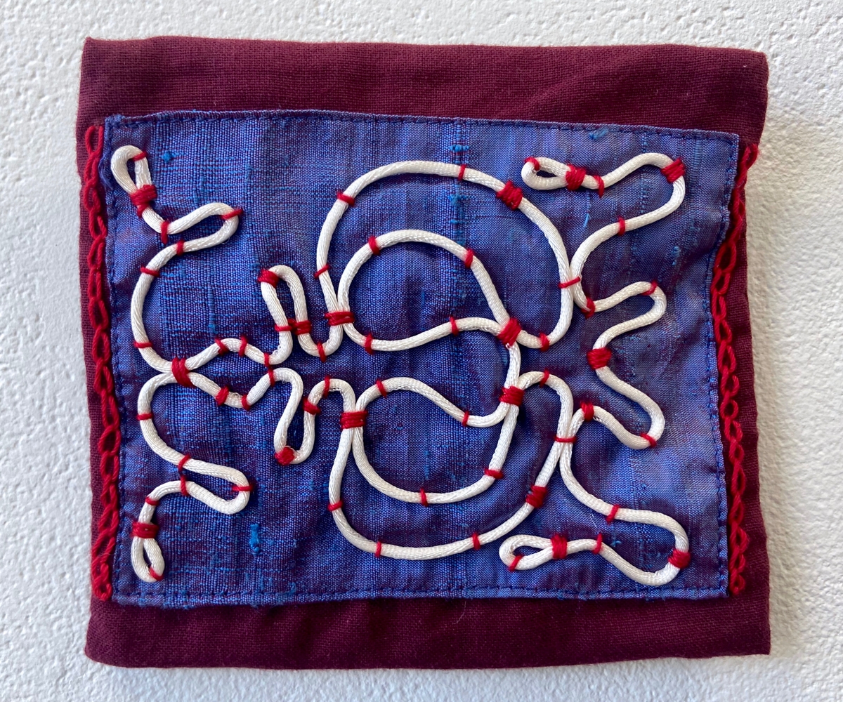 A blue fabric piece with white strict attached to it with red thread