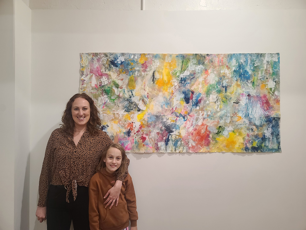 A woman poses for a photo in front of a piece of abstract art with a young girl