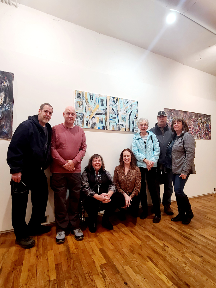 Seven people pose for a photo in front of paintings