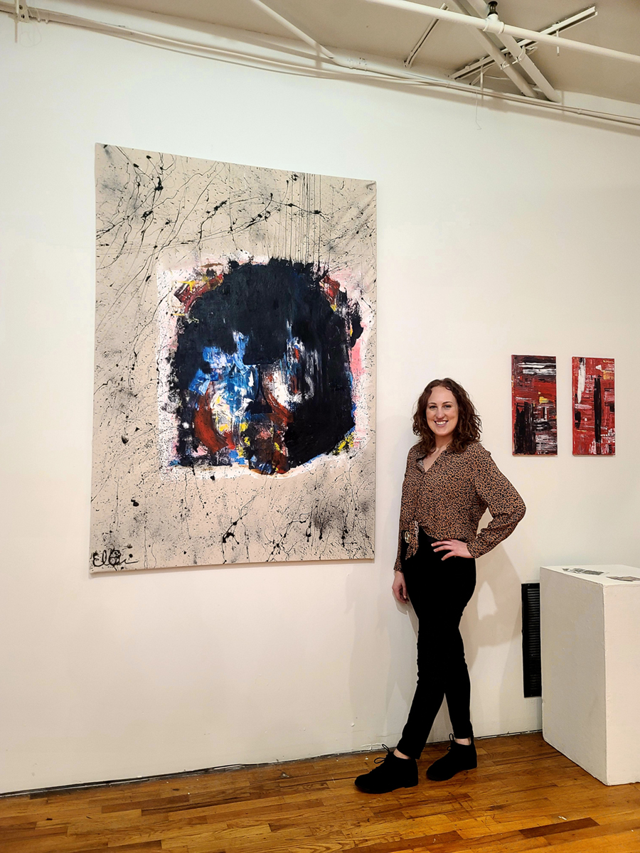 A woman poses for a photo next to one of the paintings from the installation