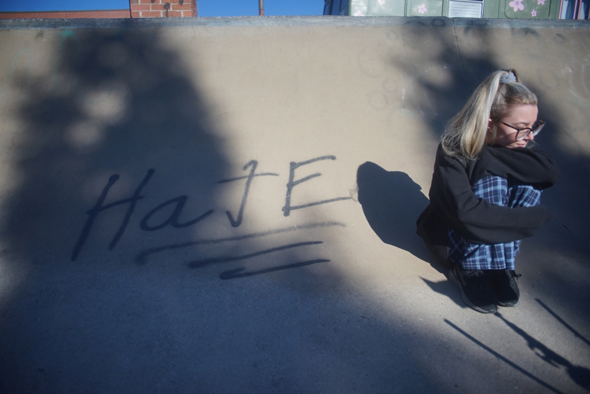 A young blonde woman sitting in a skate park with "hate" spraypainted next to her
