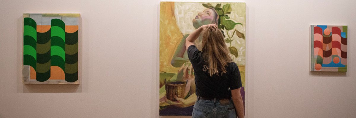 A woman looking at a painting of a woman-plant hybrid