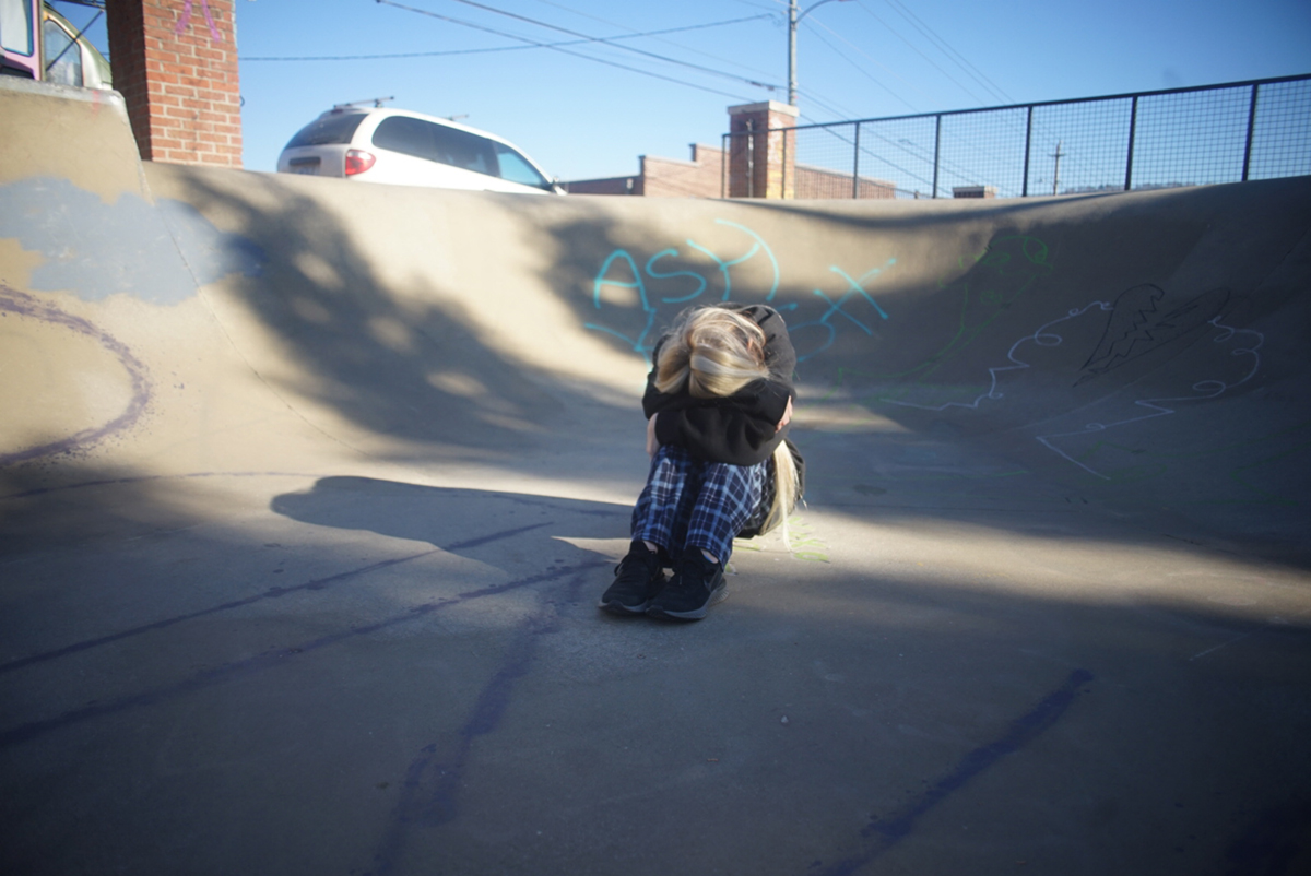 A young blonde woman sitting in a skate park, her head in her arms