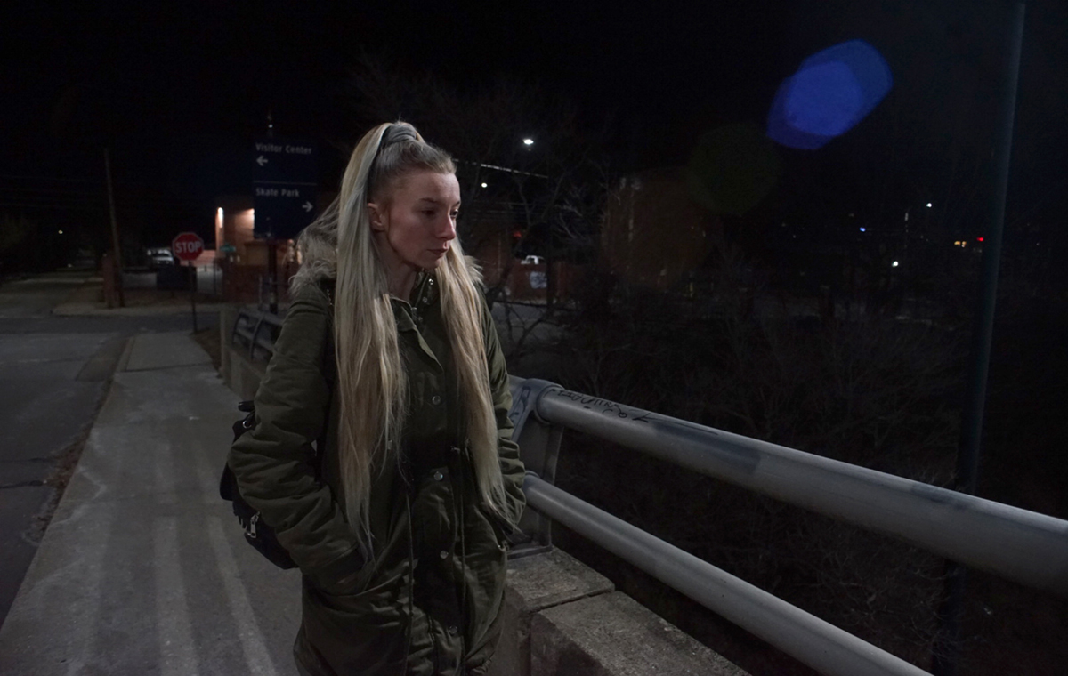 A photo of a young blonde woman walking at night