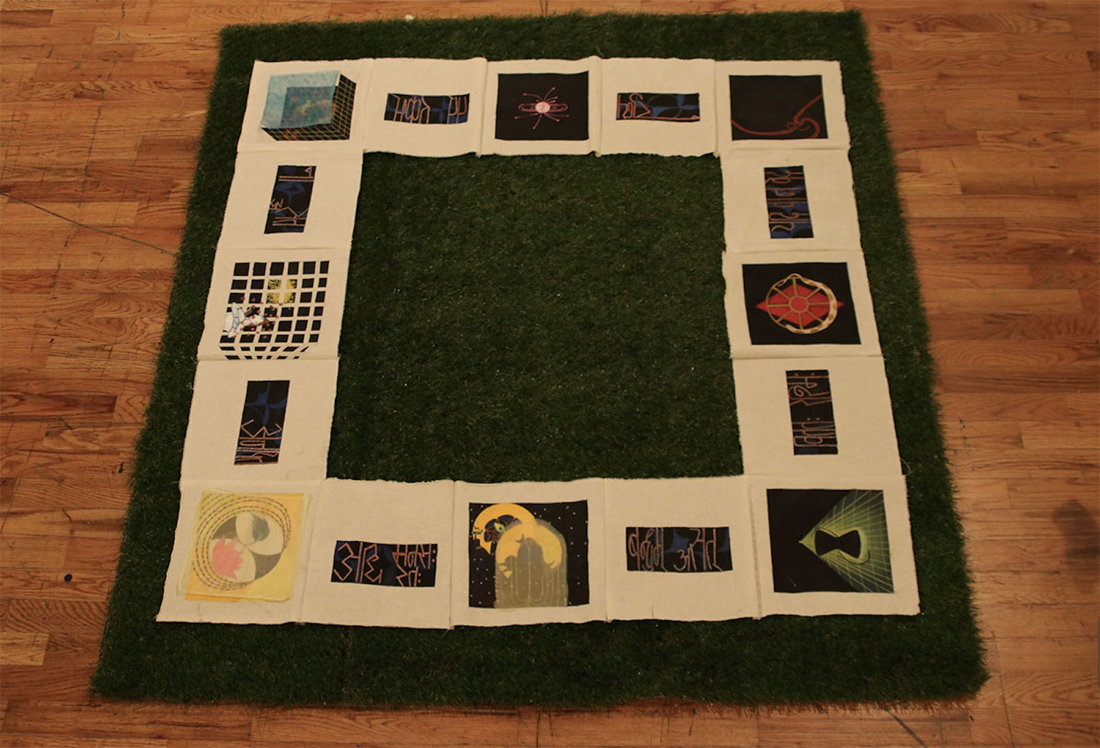 Art on square formats arranged as a border along a patch of green turf.