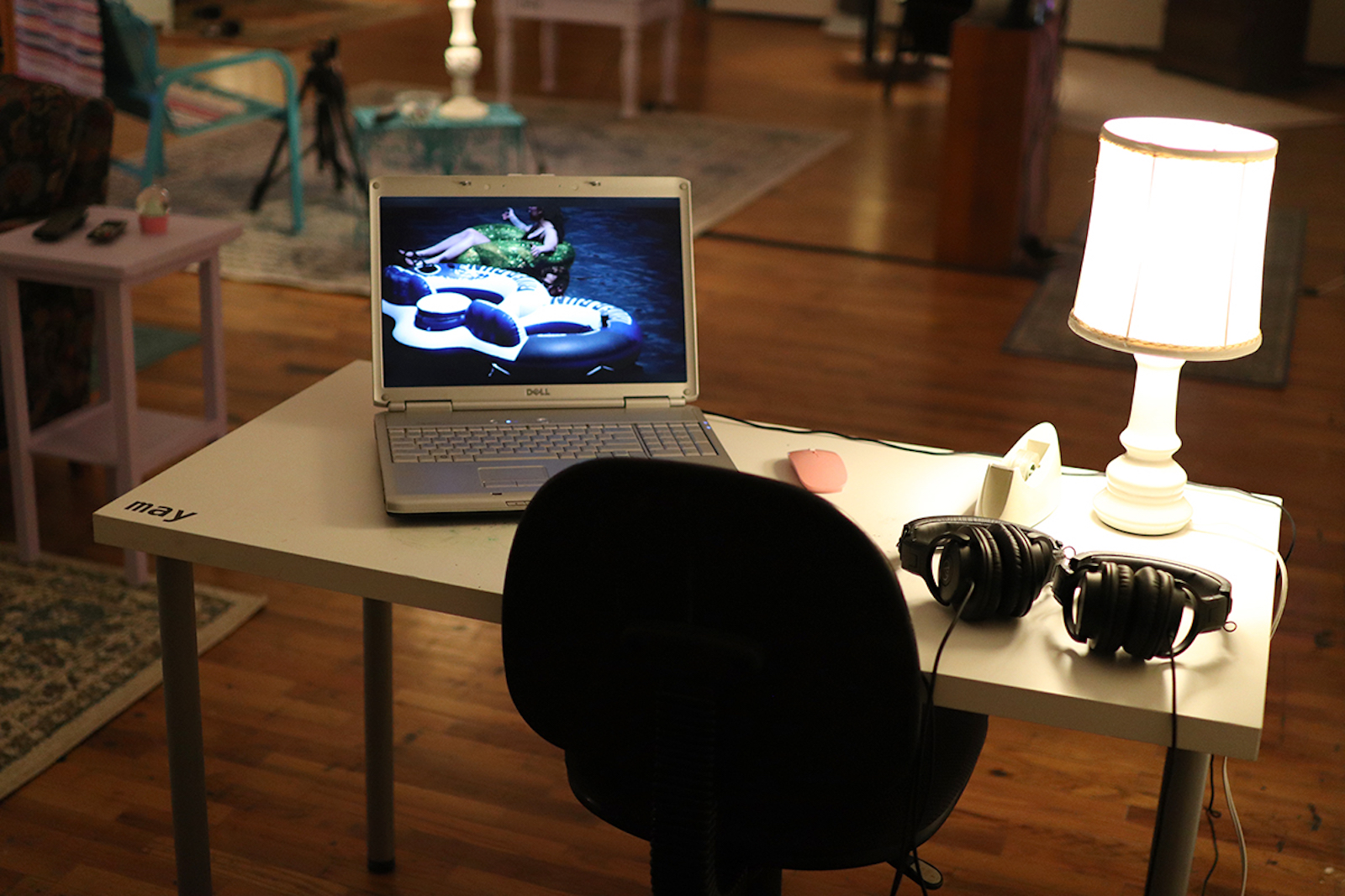 A table with a laptop, office chair, lamp, and two sets of headphones