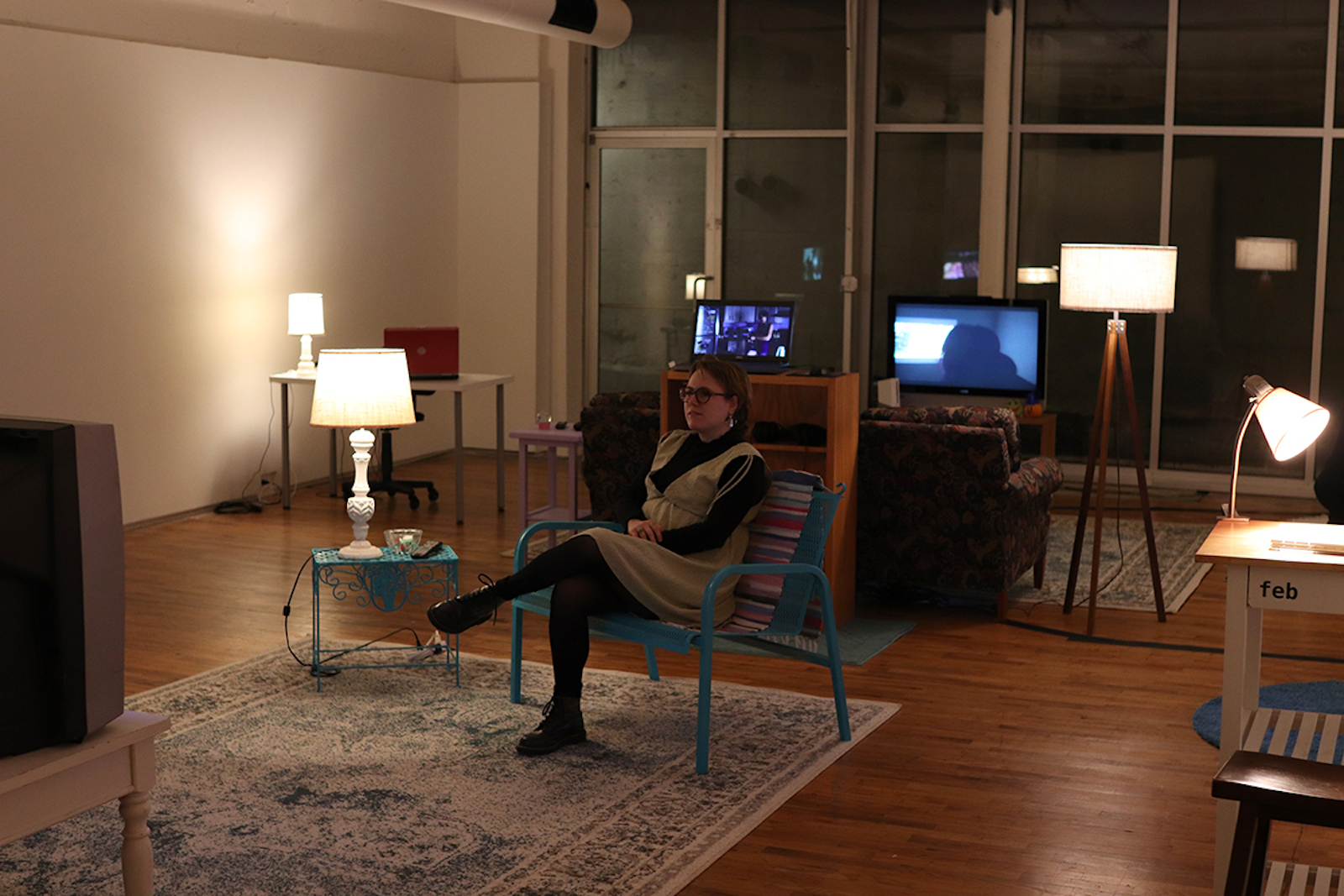 A woman sitting in a chair watching a tv, and you can see two other tvs in the background behind her