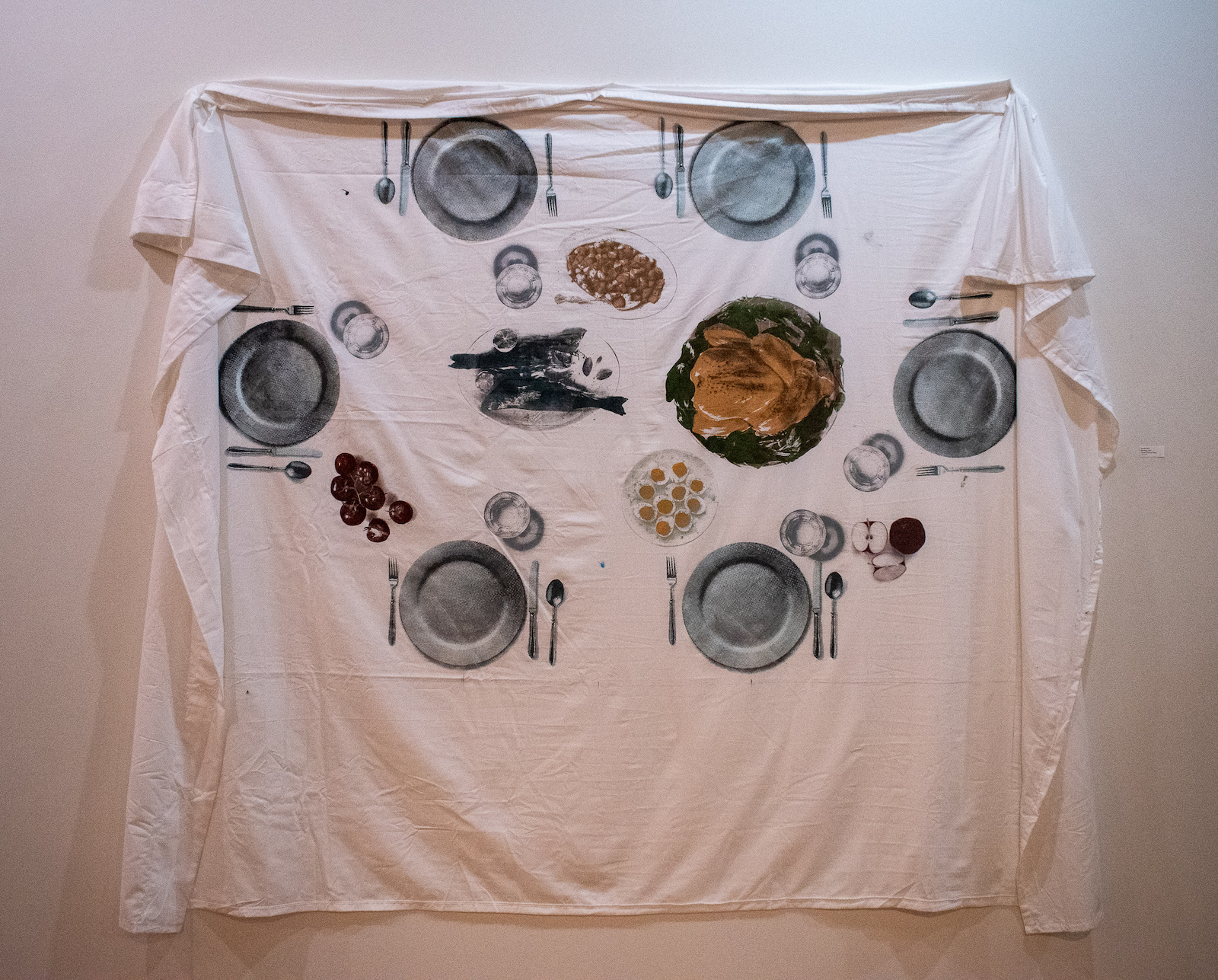 A blanket printed with an illustration of a dinner table spread hung on the wall