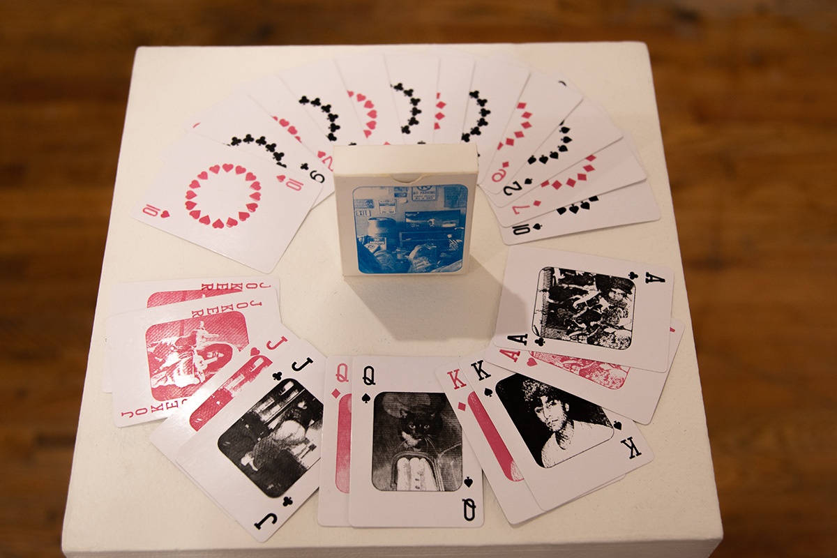 An art gallery installation featuring colorful illustrated playing cards arranged on white geometric pedestal.