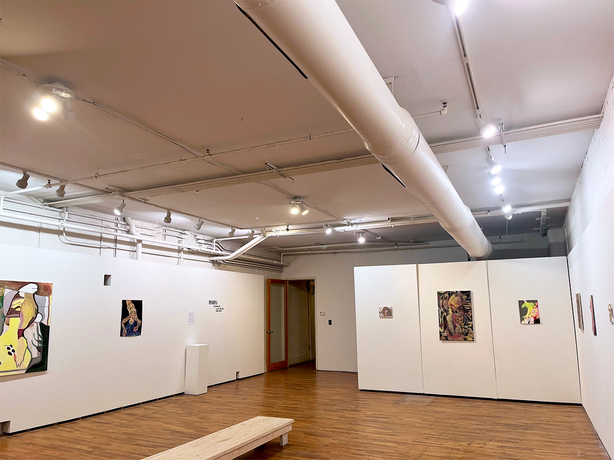 Installation view of a white gallery wall lit by track lighting, hung with three paintings at receding depth. The largest, at left, is a dense web of purple, red, and orange line work over pale figurative forms. At center, a vertical canvas in gray, black, and yellow shows abstracted facial features and dotted patterning. A small work in blue and green hangs farthest right. Wood parquet floor
