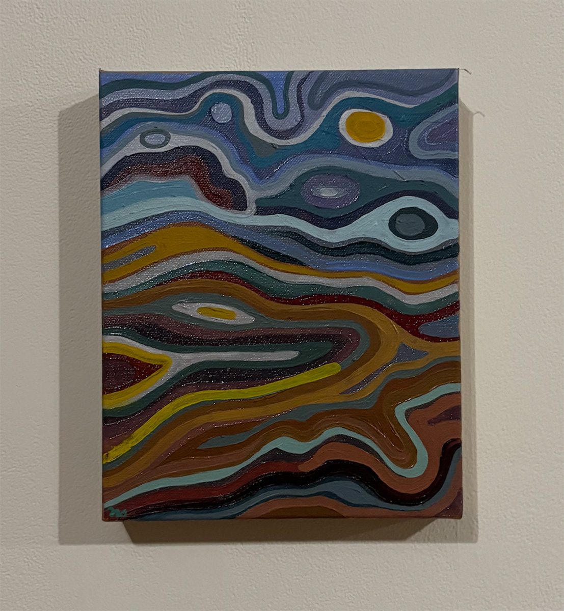 Abstract post-impressionist painting titled 'Stinson Beach' by Nolan Steil, mounted on a light-colored wall. The composition uses flowing, wavy bands of color to suggest a landscape or aerial view: the upper portion has swirling blues, grays, and purples resembling sky or water, with a yellow circular sun or moon shape and smaller dark orbs. The lower portion transitions into warm, layered bands of gold, rust, maroon, and brown resembling hills or terrain, with a bright yellow curving line running through the middle. A small signature or date mark appears in the bottom left corner of the canvas