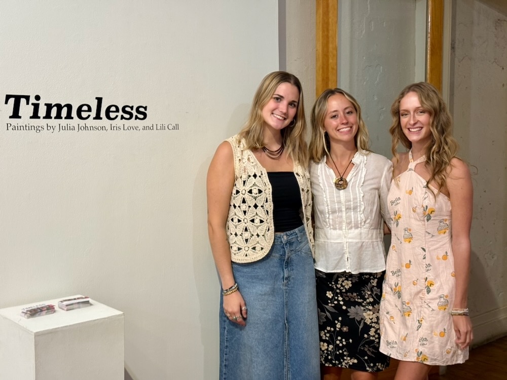 Julia Johnson, Iris Love, and Lili Call standing and smiling next to wall vinyl.