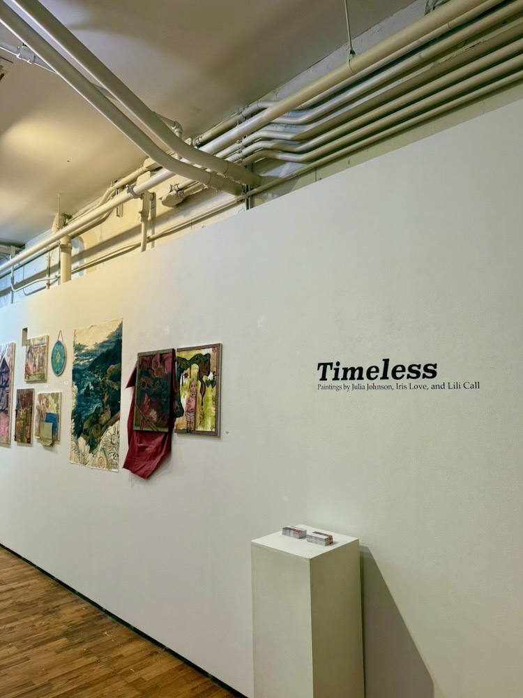 Gallery wall with paintings and a vinyl wall tag.