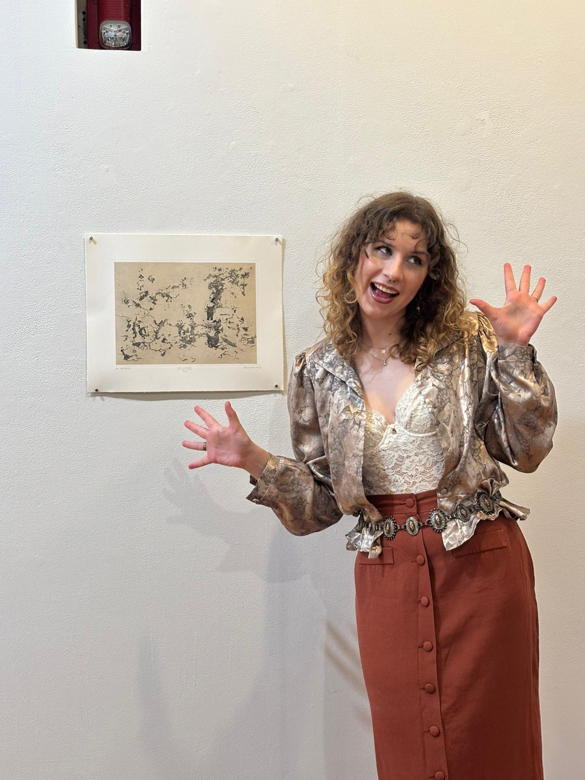 Iga Budzik where a metallic shirt and brown skirt standing next to a tan and black intaglio print on paper.