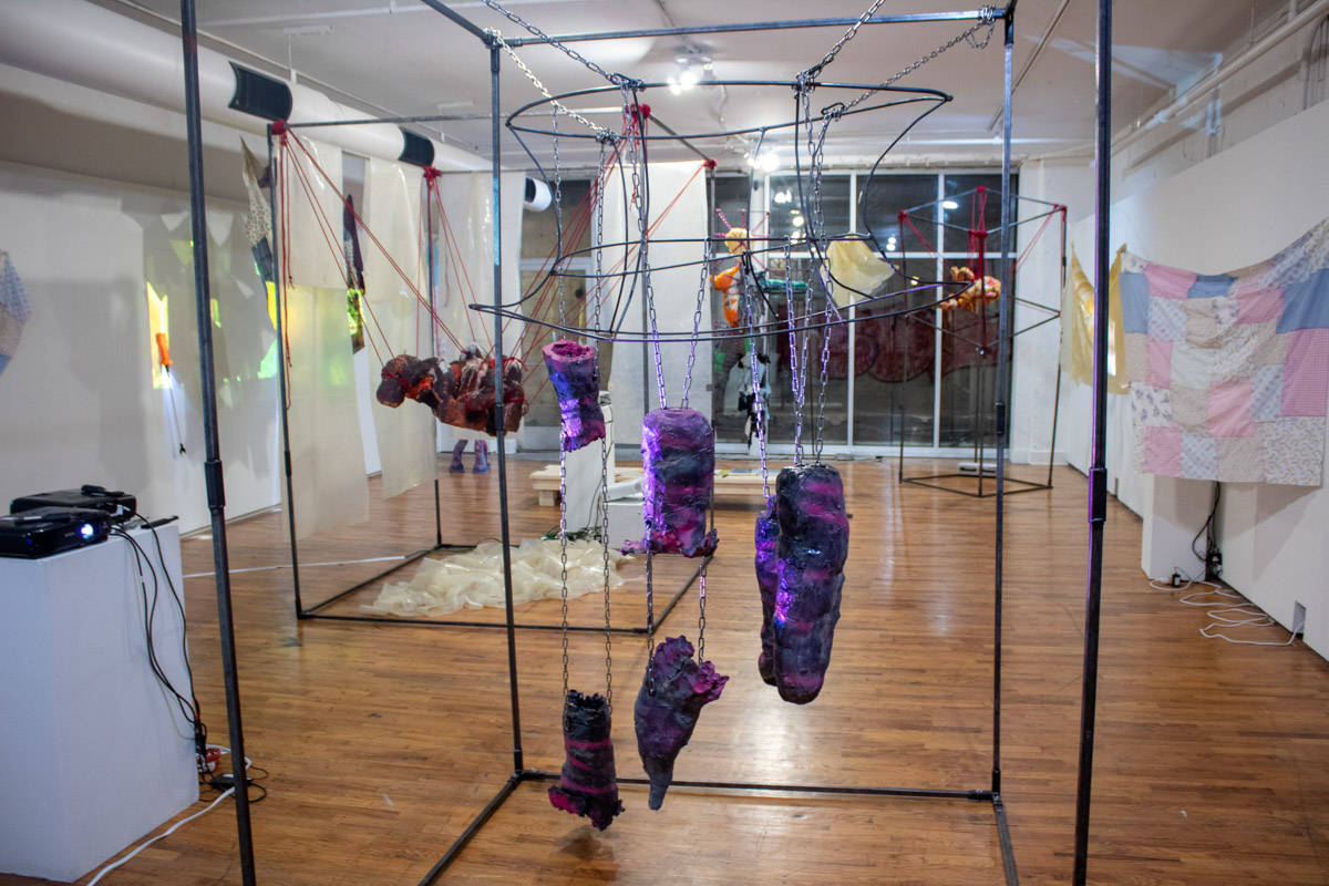 Gallery with ceramic sculptures suspended in metal frame with quilts and projections. 